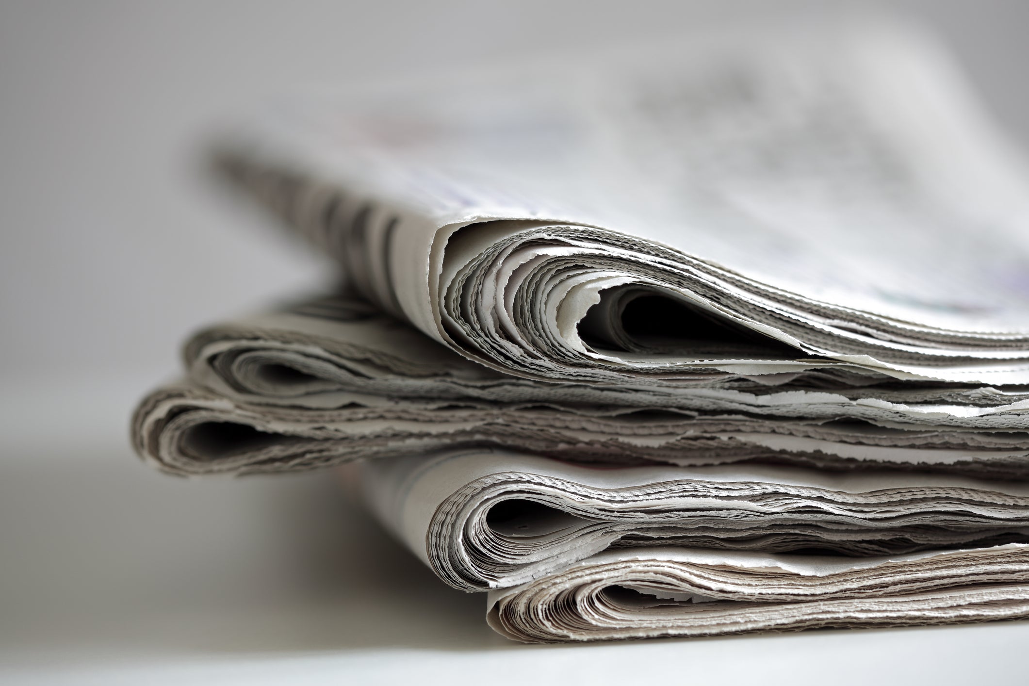 A close-up of folded newspapers stacked in a neat pile, showcasing the textures and layers of printed pages—symbolic of traditional journalism and daily news consumption.